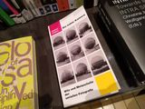 Stephan Gregory: Die kühle Kamera. Witz und Melancholie der seriellen Fotografie, tentare Verlag – Buch mit Raster aus Schwarzweißfotos kugelförmiger Gasbehälter, magentafarbenem und gelbem Farbfeld, auf einem Glastisch in einer Buchhandlung zwischen anderen Kunstbüchern