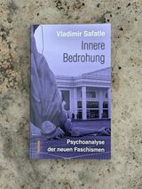 Vladimir Safatle: Innere Bedrohung. Psychoanalyse der neuen Faschismen, tentare Verlag – Buch auf hellem, fleckigem Steinboden; violett eingefärbtes Umschlagfoto einer umgestürzten Freiheitsstatuen-Nachbildung vor einem Kaufhaus