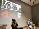 Karen van den Berg: Große Kunst. Hyperwachstum in der Studiopraxis, tentare Verlag – Buchvorstellung an der Akademie der Bildenden Künste München am 4. Februar 2026: Karen van den Berg im Gespräch mit Léa Kuhn vor einer Projektion mit historischen Fotos aus der Skulpturenfabrik Lippincott