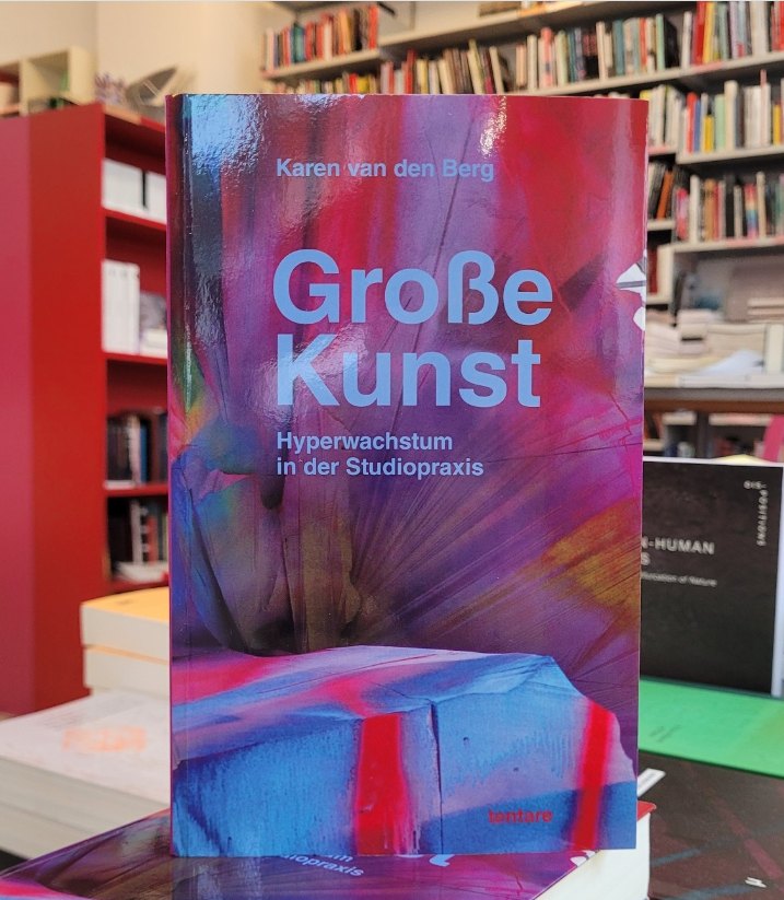Karen van den Berg: Große Kunst. Hyperwachstum in der Studiopraxis, tentare Verlag – Buch mit farbigem Cover nach Katharina Grosses Installation It Wasn’t Us, aufgestellt in der Buchhandlung pro qm in Berlin vor Bücherregalen