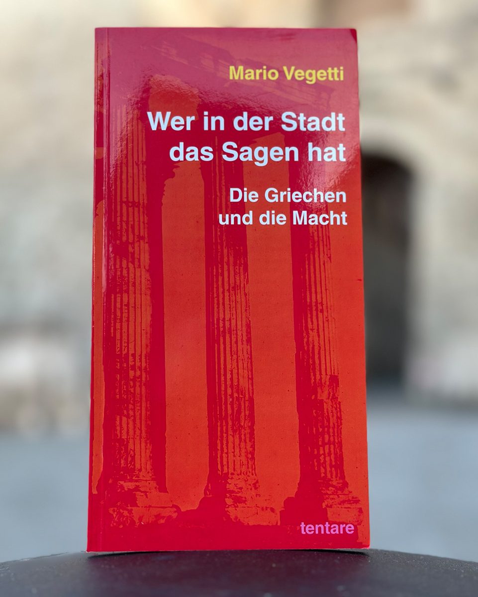 Mario Vegetti: Wer in der Stadt das Sagen hat. Die Griechen und die Macht, tentare Verlag – rotes Taschenbuch mit den Säulen eines griechischen Tempels auf dem Cover, aufrecht vor einer unscharfen Altstadtfassade mit Torbogen